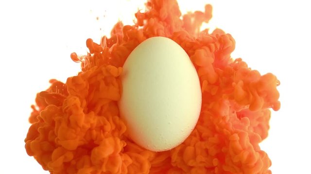 Colored fluid in motion. Orange paint pours on a white egg in water. Isolated on a white background. Design concept. Beautiful effect. Selective focus. Close up. Full HD video 1920x1078