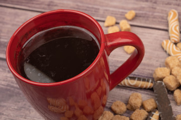 A red ceramic tea mug, cookie sticks with chocolate and white icing, and pieces of brown cane sugar on a wooden background. Close up.