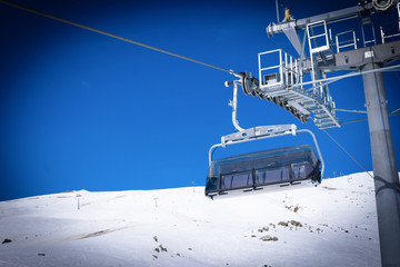 Empty chair lift and holding contructions with snowy peak in the background. Ski resort end season...