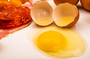 Broken chicken egg and slices of bacon and sausage on a white background. Close up.