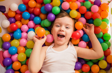 Fototapeta na wymiar Little girl lies in multicolored balls
