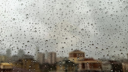 Raindrops on office window with blur grey sky background. Office window covered with closeup rain water.