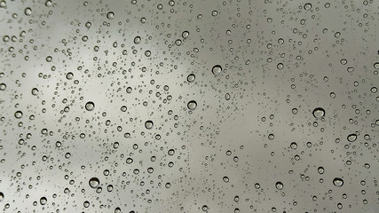 Raindrops on window view in rainy season in Turkey. Rain running down on window with cloudy sky blur light, grey color background
