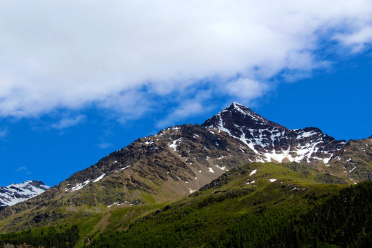 Muntain in early summer covered by forest and little snow on the top