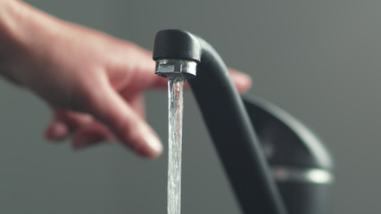 Woan is opening and closing water flow tap and filling sink with water. Water running from chrome...