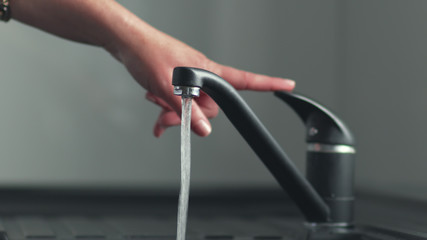 Woan is opening and closing water flow tap and filling sink with water. Water running from chrome...