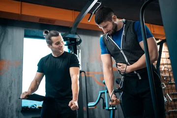 Gordijnen young man has workout with personal trainer in modern gym © goami