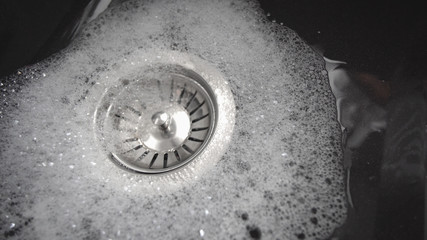 Water is running from open faucet into black granitte sink, closeup