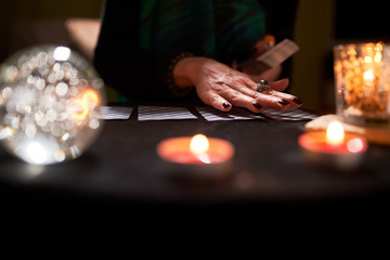 Woman fortune-teller's hands, fortune-telling cards, ball of predictions on black table