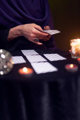 Fortune teller in purple dress divines on cards sitting at table with candles