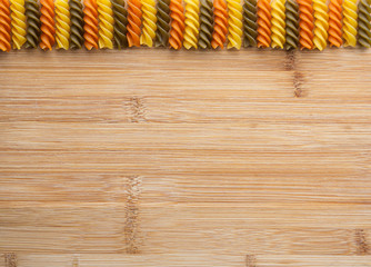 Raw multicolored tricolore fusilli pasta scattered on brown wooden background. Horizontal banner....