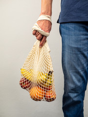 Obraz premium Mann über 40 hält ein Einkaufsnetz mit frischen Obst in seiner Hand, nachhaltige Lebensweise, Umwelttheme, wiederverwendbare Einkaufstasche
