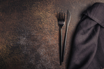 Elegant black table setting: napkin and silverware over dark background. Flat lay. Top view.