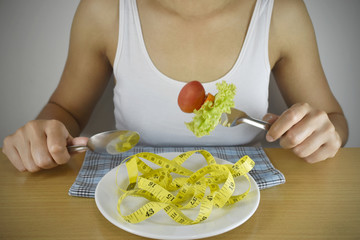 Healthy lifestyle concept. female hand holding fork with healthy food and measuring tape over the plate.
