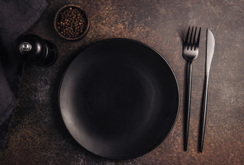 Elegant black table setting: plate, napkin and silverware over dark background. Flat lay. Top view.