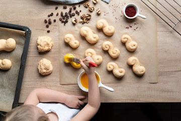 Preparation homemade bread rolls by little girl for brakfast on the wooden table in a kitchen. Handmade food and delicious bread-baking. Bakery at home. Fun for children. Top view.