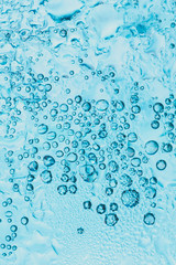 transparent background of soda water and ice with bright blue bubbles within the glass