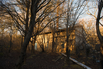 Abandoned burned old house in winter at sunset in forest. Abandoned hunting lodge in the warm rays of the sun in the middle of the forest.