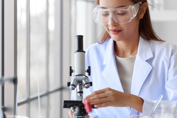 Young attractive Asian woman scientist wearing white lab coat using microscope in laboratory room.