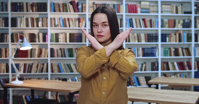 Portrait of angry brunette girl crossing her hends and saying no in library.