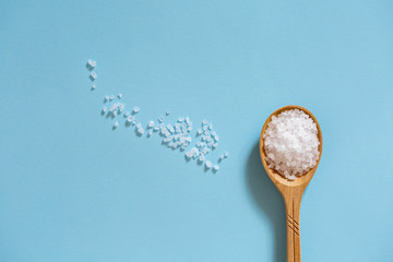 Coarse sea salt in a wooden spoon on a blue background. Ingredient for cooking and spa treatments.