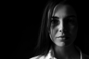 Black and white portrait of scared female victim on dark background. Concept of violence