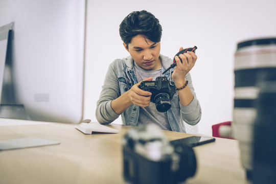 Asian Photographer cleaning blowing the dust from his camera in studio - Powered by Adobe