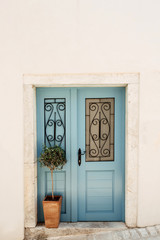 Fototapeta na wymiar Typical European house. Old blue carving door, white wall, green plant in square terra-cotta pot.