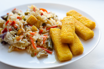 frying fish sticks in a pan. Homemade breakfast. Rice with vegetables and fried fish sticks.