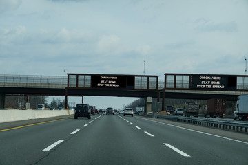 Electronic information sign over a busy multi-lane highway that says Coronavirus stay home to stop the spread