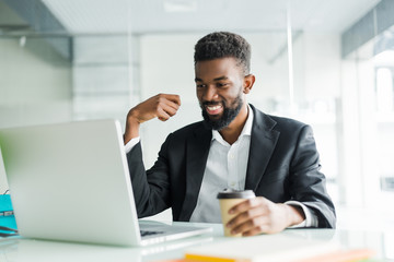 Young African American manager with stubble sitting in front of open laptop wearing earphones while having video conference call with business partners