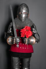 A medieval warrior in armor holds a sword and flowers in his hands. A knight gives a bouquet of roses.