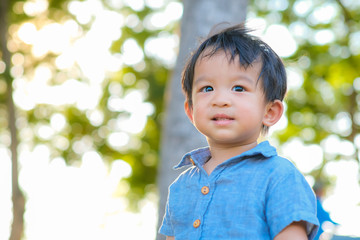 Happy little boy in the blue shirt standing on green grass field in city park