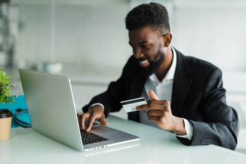 Internet banking sales. Successful African businessman sitting at a laptop and holding credit card in hand until businessman doing orders through the Internet