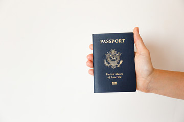 Macro shot of woman's hand holding the latest version of United States of America citizen Passport with biometric ID chip. Person identification document. Close up, copy space, white wall background.