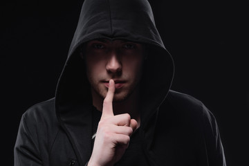 A man in a black hood on a black background, studio photography. The idea of mysticism, mystery,...