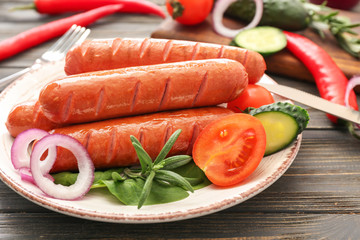 Plate with tasty grilled sausages and vegetables on table