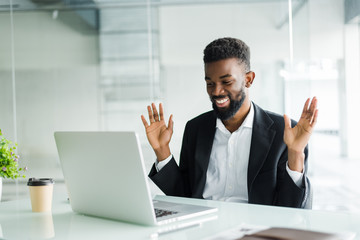 Shocked african-american businessman in suit feeling stunned by online news looking at computer...