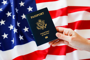Macro shot of woman's hand holding the latest version of United States of America citizen Passport with biometric ID chip. Person identification document. Close up, copy space, USA flag background.