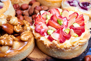 Mini tarts cupcakes with strawberries, walnuts, almond, nuts and blueberries on blue wooden background. Close up