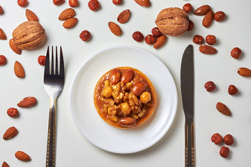 Mini tart cupcake with walnuts, almonds and hazelnuts on plate with knife and fork. Close up. Top view