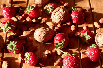 Strawberries, walnuts, hazelnuts and almonds on a wooden background in the sun