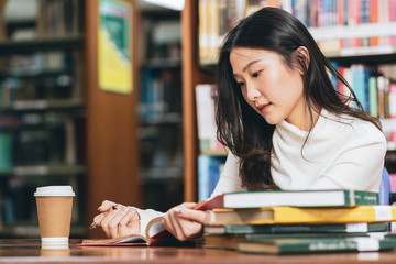 Young beautiful asian student girl working a book, learning in college library in university