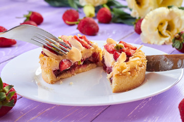 Knife and fork cutting mini tart cupcake with strawberries on plate. Close up.