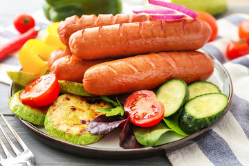 Plate with tasty grilled sausages and vegetables on table