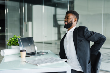Young businessman in office at desk suffering from back pain in office