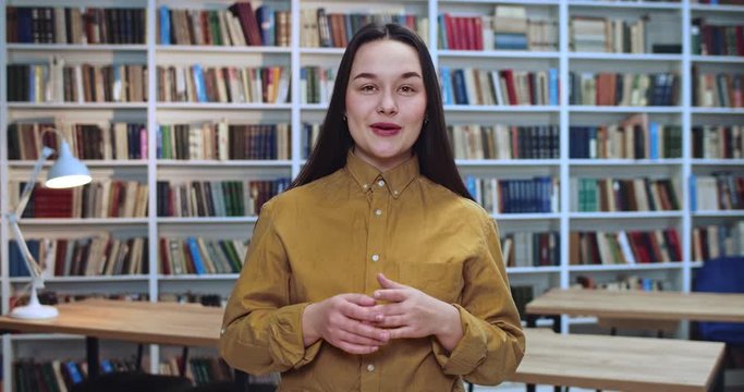 Portrait of happy active female student emotionally speaking and making a lot of gests by her hands in library.