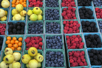 boxes of berries, yellow tomatoes and passionfruit on display for sale at a market stall at the...