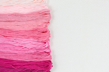 skeins of embroidery threads in shades of pink on white cotton canvas