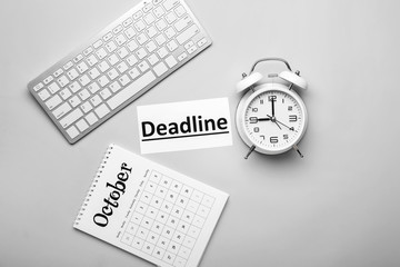 Calendar with computer keyboard, alarm clock and word DEADLINE on grey background